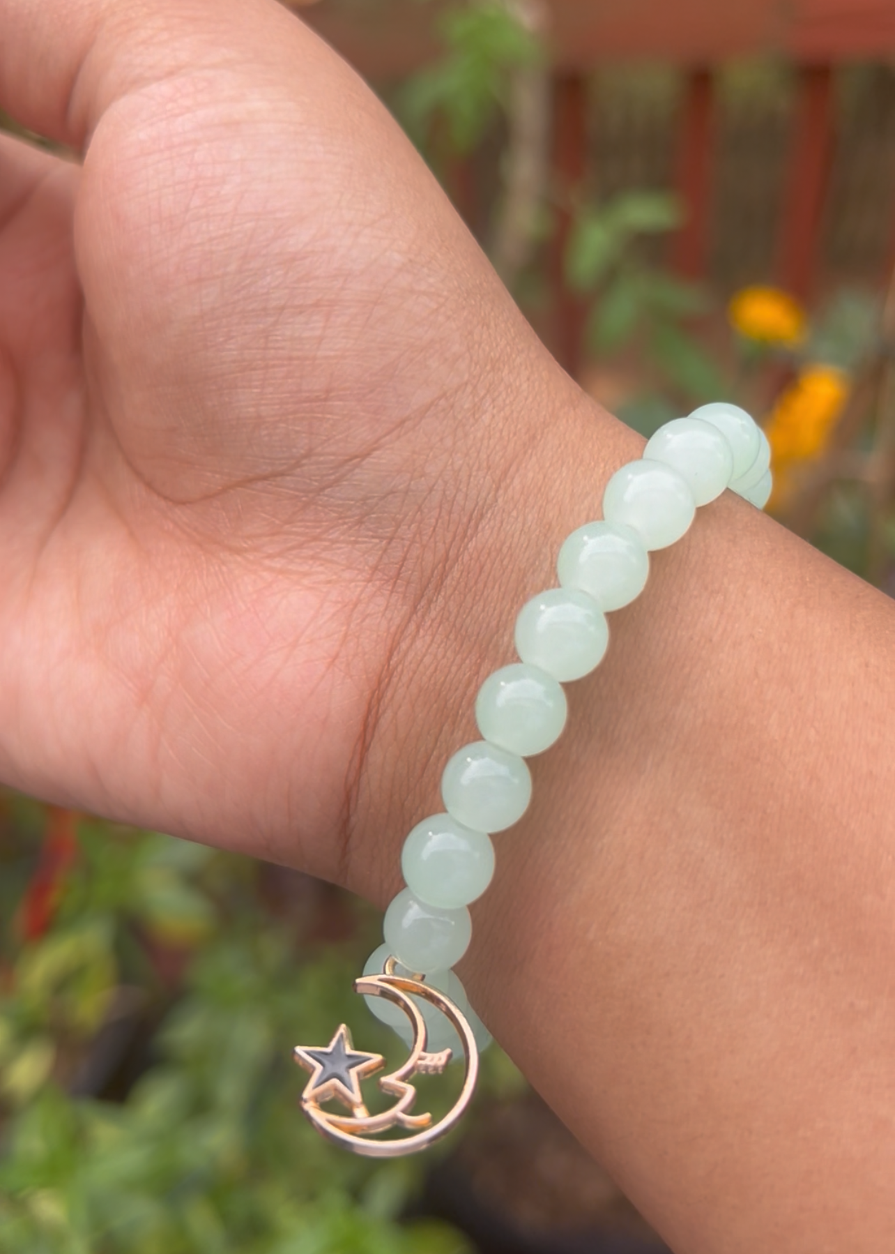 Hand wearing a bracelet with a moon and star charm against a blurred natural background