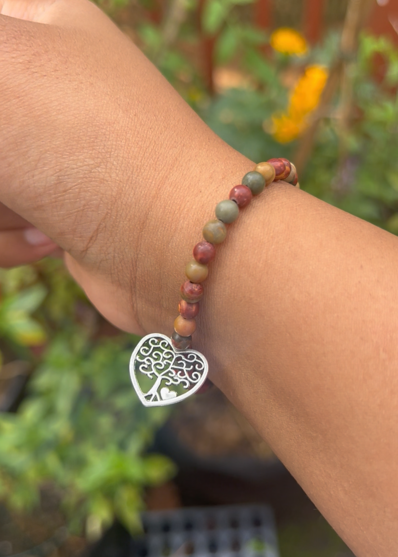 Bracelet with a tree-shaped charm on a wrist against a blurred outdoor background